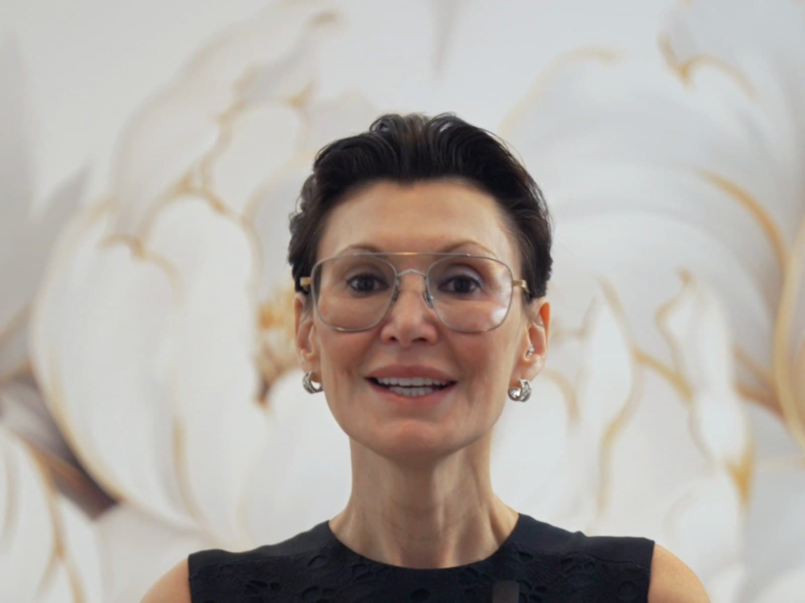 Victoria Karlinsky, MD, smiling in front of a cream floral wall at Alluring Plastic Surgery in Miami